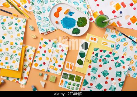 Overhead-Papierblätter mit verschiedenen Ornamenten und Paletten mit Flecken Von Farbe auf orangefarbenem Hintergrund angeordnet Stockfoto