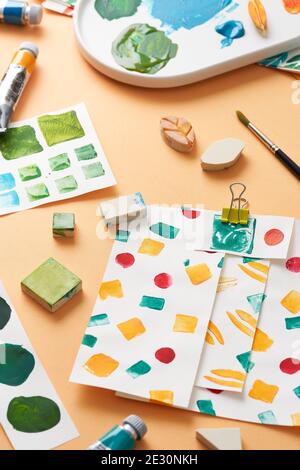 Verschiedene geometrische Stempel und Palette mit Farbe auf Orange platziert Hintergrund in der Nähe von Papierblättern mit Ornamentmustern Stockfoto