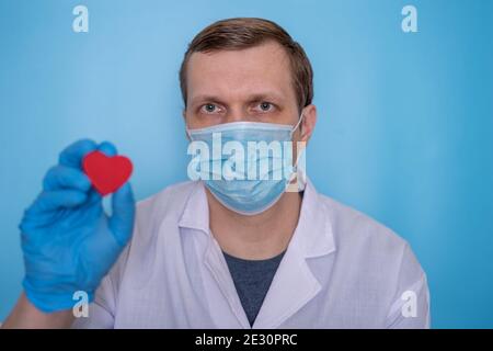 Ein Chirurg in einem weißen Mantel hält mit einer Hand ein Spielzeug-Herz auf einem hellblauen Hintergrund. Das Konzept der Medizin und Gesundheitsversorgung. Stockfoto