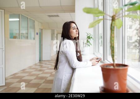 Ärztin mit Stethoskop und Handy in der Klinik In der Nähe des Fensters Stockfoto