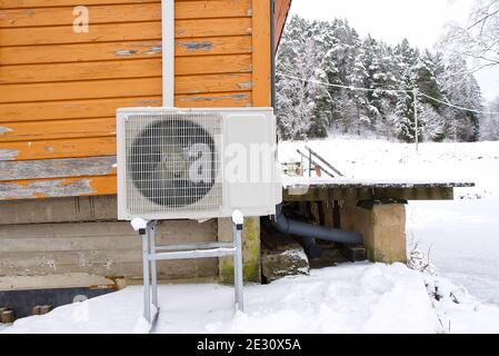 Luft-Wasser-Wärmepumpe in der Nähe eines alten Holzhauses im Winter. Luft-Wasser-Wärmepumpe aus nächster Nähe Stockfoto