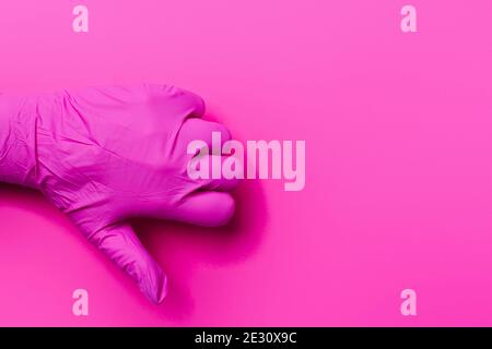 Eine Hand eines Sanitäters in einem rosa Handschuh zeigt eine Abneigung auf einem rosa Hintergrund mit Seitenraum. Daumen nach unten. Stockfoto