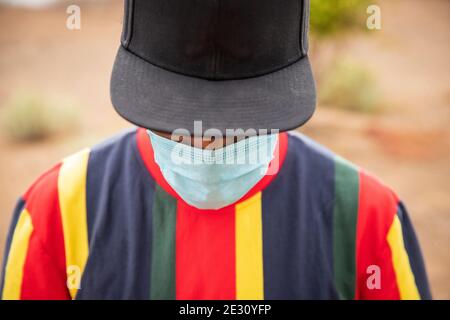 Junger schwarzer Kerl mit Schutzmaske und schwarzem Hut Während der Covid-19-Pandemie Stockfoto