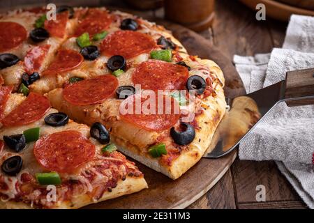 Nahaufnahme einer Scheibe Pepperoni Pizza mit Oliven und Paprika auf einem Backstein Stockfoto