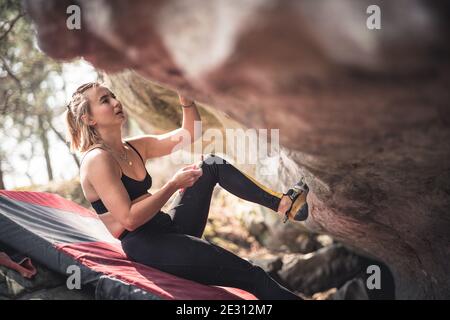 Eine starke Frau bereitet sich darauf vor, einen überhängenden Felsbrocken beim Bouldern in Fontainebleau, Frankreich, zu besteigen Stockfoto