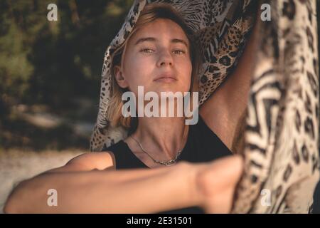 Eine junge Frau mit blondem Haar schattiert sich mit einem Schal mit Leopardenmuster vor der Sonne. Stockfoto