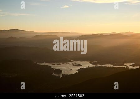 Helles goldenes Sonnenlicht am Morgen. Horizont über der Bergkette mit atemberaubendem orangefarbenem Licht bei Sonnenaufgang. Maskeliya Stausee im Tal. Panoramablick Stockfoto