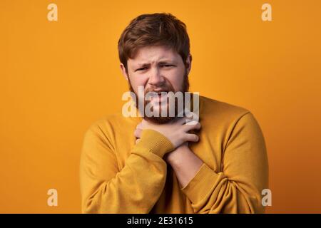 Foto von müde bärtigen Mann mit negativem Gesichtsausdruck, leidet an Ersticken, hält die Hände auf den Hals, sieht in Unmut bei der Kamera, hat Ingwer Stockfoto