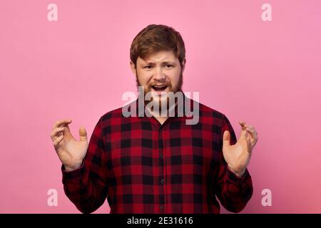 Schockiert peinlich junger Mann zeigt etwas sehr riesig, Schnappatmung vor Wunder, misst großen Gegenstand mit beiden Händen, trägt lässige gelbe T-Shirt, s Stockfoto