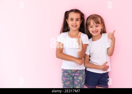 Kinder zeigen wie. Zwei liebenswert glücklich kleine Mädchen gestikuling Daumen nach oben zusammen und lächeln zur Kamera, ausgezeichnetes Feedback, gute Arbeit. Indoor-Studio Stockfoto