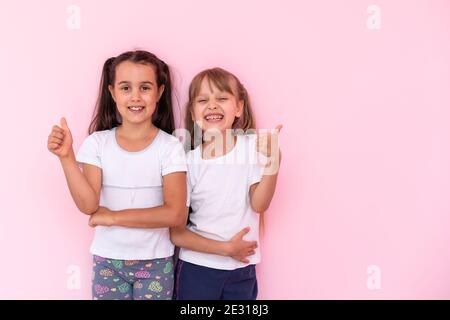 Kinder zeigen wie. Zwei liebenswert glücklich kleine Mädchen gestikuling Daumen nach oben zusammen und lächeln zur Kamera, ausgezeichnetes Feedback, gute Arbeit. Indoor-Studio Stockfoto