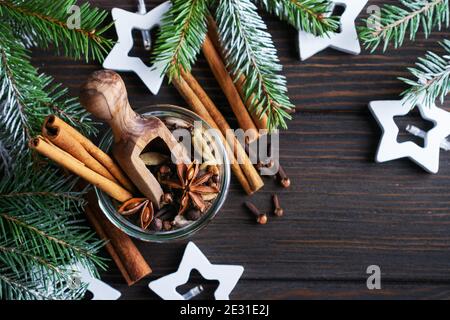 Mischung aus Glühweingewürzen in einem Glas Anis, Kardamom, Piment, Zimtstangen, Nelken auf dunklem Holzgrund. Für Text platzieren. Stockfoto