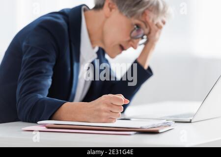 Verschwommene Geschäftsfrau mittleren Alters mit geballter Faust, die unter Kopfschmerzen leidet Im Büro Stockfoto