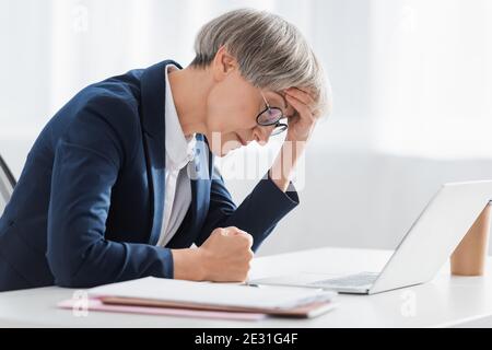 Erschöpfte Geschäftsfrau mittleren Alters leidet Kopfschmerzen im Büro Stockfoto