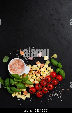 Italienische Pasta Orecchiette mit traditionellen Zutaten für die Zubereitung von Speisen auf schwarzem Hintergrund. Kulinarisches Essen Kochen Hintergrund. Draufsicht. Stockfoto