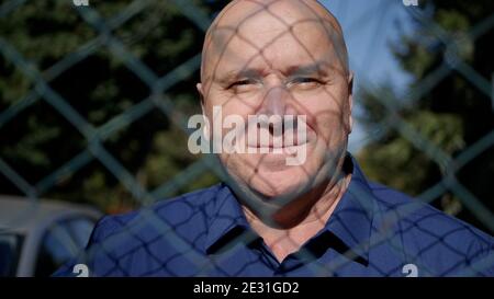 Bild mit einer älteren Person hinter einem metallischen Zaun lächelnd Glücklich Stockfoto