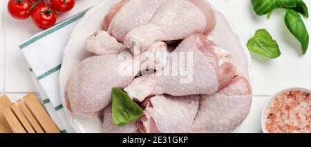 Rohe Hähnchenbeine mit Tomatenkirsche, Kräutern, Basilikum und Gewürzen, auf weißem Marmorhintergrund, Kopierraum Draufsicht. Kochen gesunde Ernährung Mittagessen Konzept. Stockfoto