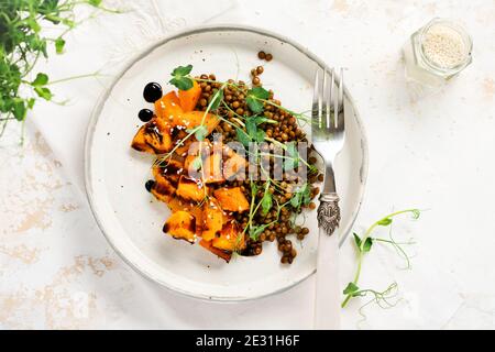 Salat mit gebackenem Kürbis, Linsen und Balsamico-Dressing garniert mit Erbsen-Microgreens auf hellem Hintergrund. Gesundes veganes Essen, Draufsicht. Stockfoto