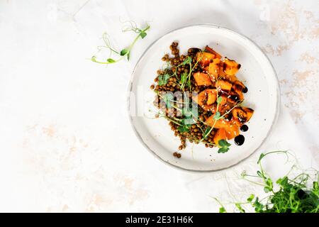 Salat mit gebackenem Kürbis, Linsen und Balsamico-Dressing garniert mit Erbsen-Microgreens auf hellem Hintergrund. Gesundes veganes Essen, Draufsicht. Stockfoto