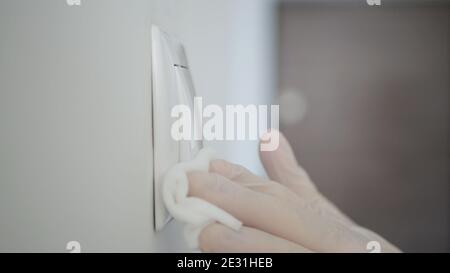 Mann trägt Schutzhandschuhe, Reinigung und Desinfektion Licht Schalter aus dem Büro mit Desinfektionsmittel gegen Covid-Viren. Quarantäne in Pandemie Stockfoto