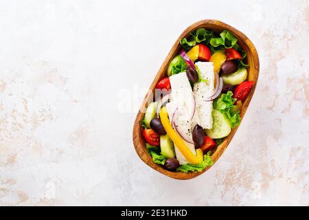 Griechischer Salat in Holzplatte auf weißem Hintergrund. Traditionelles griechisches Gericht. Selektiver Fokus. Draufsicht. Stockfoto