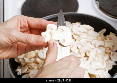 Closeup kocht Hände mit Küchenmesser, das Champignon-Pilze in einer Pfanne in dünne Scheiben schneidet. Geringer Fokus. Stockfoto