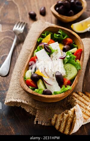 Griechischer Salat in Holzplatte auf altem Holzhintergrund. Traditionelles griechisches Gericht. Selektiver Fokus. Draufsicht. Stockfoto