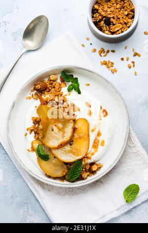 Griechischer Joghurt mit karamellisierter Birne, Müsli, Nüssen und geschmolzenem Zucker für ein gesundes Frühstück auf einer grauen Keramikplatte. Rustikaler Stil. Draufsicht. Stockfoto