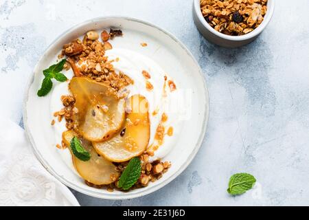 Griechischer Joghurt mit karamellisierter Birne, Müsli, Nüssen und geschmolzenem Zucker für ein gesundes Frühstück auf einer grauen Keramikplatte. Rustikaler Stil. Draufsicht. Stockfoto