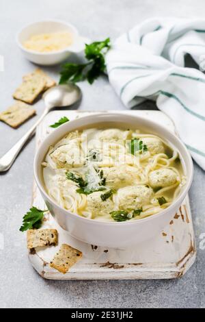 Suppe mit Hühnerfleischbällchen und Eierpaste, Parmesankäse, Petersilie in einer Keramikschale auf grauem Tischhintergrund. Traditionelle italienische Brühe. Draufsicht. Stockfoto