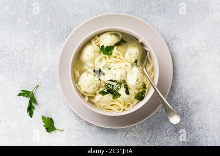 Suppe mit Hühnerfleischbällchen und Eierpaste, Parmesankäse, Petersilie in einer Keramikschale auf grauem Tischhintergrund. Traditionelle italienische Brühe. Draufsicht. Stockfoto