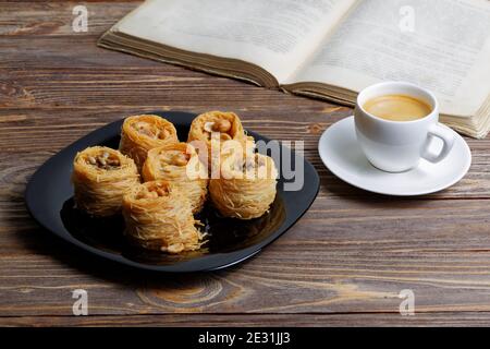 Tasse Kaffee Espresso und östlichen Süßigkeiten auf Holztisch. Buch auf verschwommenem Hintergrund öffnen. Stockfoto