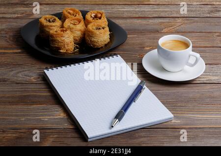 Öffnen Sie Notizbuch, Stift, Tasse Kaffee Espresso und östlichen Süßigkeiten auf Holztisch Stockfoto