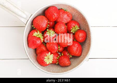 Gereinigte rote reife Erdbeeren in einem alten Metallsieb mit Wassertropfen auf weißem Holztisch. Draufsicht. Stockfoto