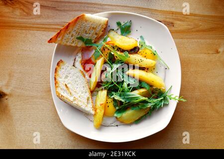 Spiegeleier mit gebratenen Kartoffelscheiben, Speck und frischer Rucola auf Holztisch. Draufsicht. Stockfoto