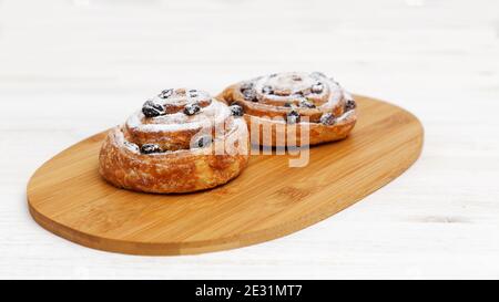 Zwei Zimtbrötchen mit Rosinen, bestreut mit Puderzucker auf Holzbrett. Geringer Fokus. Stockfoto