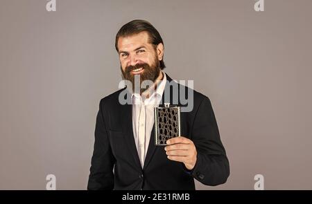 Wirklich guter Geschmack. Flache Metallflasche für Alkohol. Mann mit elegantem Look. Bärtiger Hipster im Anzug halten Metallflasche für Alkohol. Alkoholgetränk Konzept. Trinken Sie Alkohol mit. Immer bei mir. Stockfoto