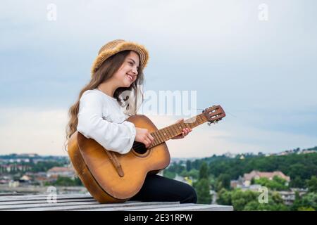 Country-Musik-Konzept. Kind Mode-Stil. Voller Inspiration. Freiheit und Erfolg. Sänger. Happy teen Mädchen Gitarre spielen im Freien. Glückliche Kindheit. Hübsches Kind auf Himmel Hintergrund. Stockfoto