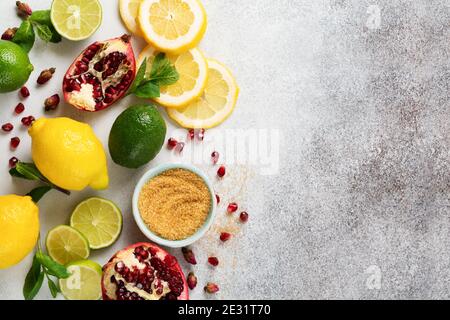 Frische Zitrone, Limette, Granatapfel, getrocknete Teesrosenblüten, Tee, Rohrzucker und Blätter Minzbukett auf grauem Hintergrund. Zutaten für die Herstellung von Limonade dr Stockfoto
