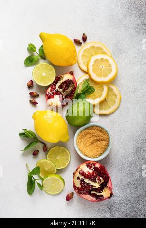 Frische Zitrone, Limette, Granatapfel, getrocknete Teesrosenblüten, Tee, Rohrzucker und Blätter Minzbukett auf grauem Hintergrund. Zutaten für die Herstellung von Limonade dr Stockfoto