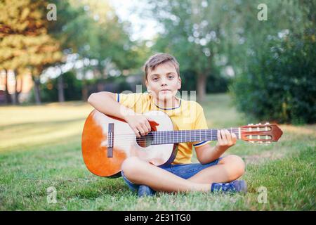 Schwer zu hören preteen junge spielen Gitarre im Freien. Kind mit Hörgeräten in den Ohren, das im Park Musik spielt und singt. Hobby Kunst Aktivität Stockfoto