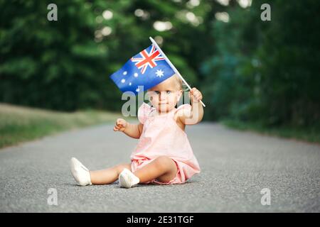 Niedlich liebenswert kaukasischen Baby Mädchen winkt australische Flagge. Lächelndes Kind, das auf der Straße im Park sitzt und den Australia Day feiert. Feiern Stockfoto