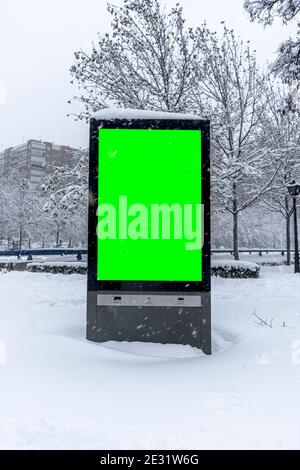 Vertikale Mock-up der Stadt Plakat Winterstadt mit dicken Kanten, grüne Plakatwand in städtischen Einstellungen, leere Straßeninformation Platzhalter auf Bürgersteig mit Stockfoto