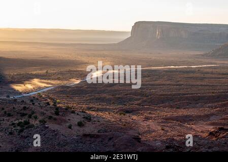 Staub, der bei Sonnenaufgang im Monument Valley Navajo Tribal Park, Arizona und Utah, USA, von Fahrzeugen über die Wüstenstraße geschleudert wird Stockfoto