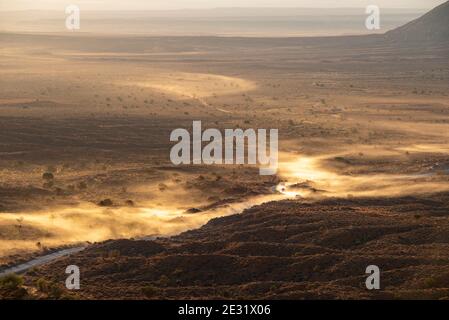 Sonnenlicht, das Staub auffängt, der von Fahrzeugen, die bei Sonnenaufgang über die Wüstenstraße fahren, im Monument Valley Navajo Tribal Park, Arizona und Utah, USA, aufgeworfen wird Stockfoto