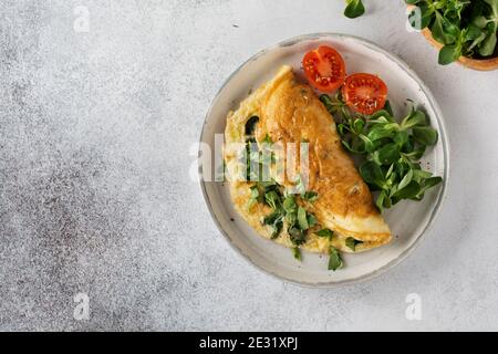 Gefülltes Omelett mit Tomaten, rotem Paprika, Frischkäse und Mais oder Lammsalat auf hellem Beton-Hintergrund mit Kopierfläche. Gesunde Ernährung für Stockfoto