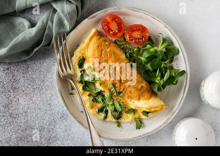 Gefülltes Omelett mit Tomaten, rotem Paprika, Frischkäse und Mais oder Lammsalat auf hellem Beton-Hintergrund mit Kopierfläche. Gesunde Ernährung für Stockfoto