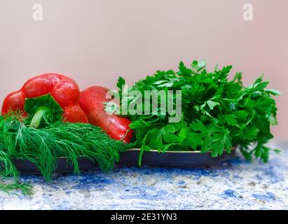 Zwei rote Paprika mit grünem Dill und Petersilie auf dem Tisch. Zutaten für Salat oder Essen. Rohes Gemüse und Kräuter. Speicherplatz kopieren Stockfoto