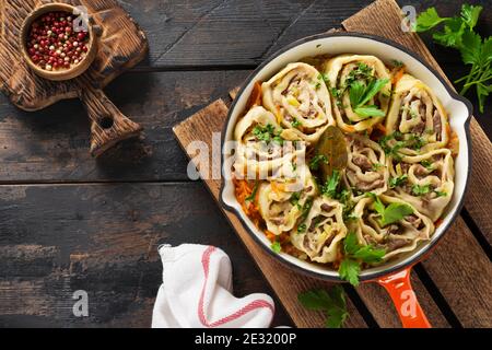 Fleischteig rollt mit Fleisch oder "faulen Knödeln" in einer gusseisernen Pfanne auf einem alten rustikalen Holzhintergrund. Draufsicht. Stockfoto