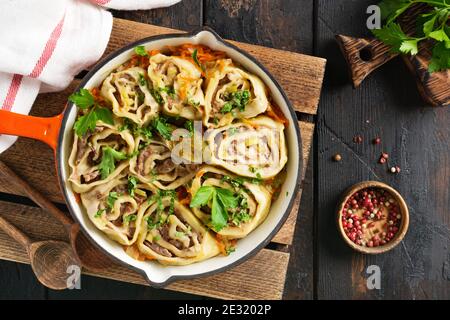 Fleischteig rollt mit Fleisch oder "faulen Knödeln" in einer gusseisernen Pfanne auf einem alten rustikalen Holzhintergrund. Draufsicht. Stockfoto